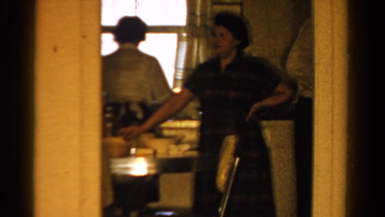 1958 Ontario kitchen scene with a woman near the counter and another adult seen from behind against the bright window.