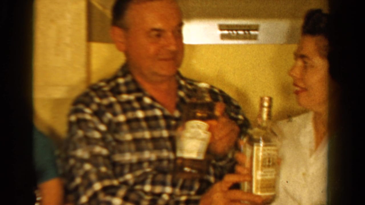 1958 Ontario kitchen frame with a man in a checkered shirt holding a cup as a woman in a white blouse smiles with a clear bottle.