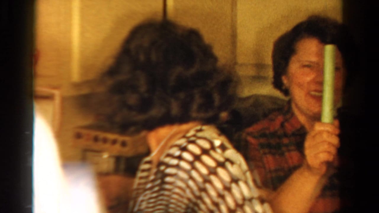 In an Ontario home kitchen, adult women laugh together while holding celery sticks, with cabinets and a counter behind them.