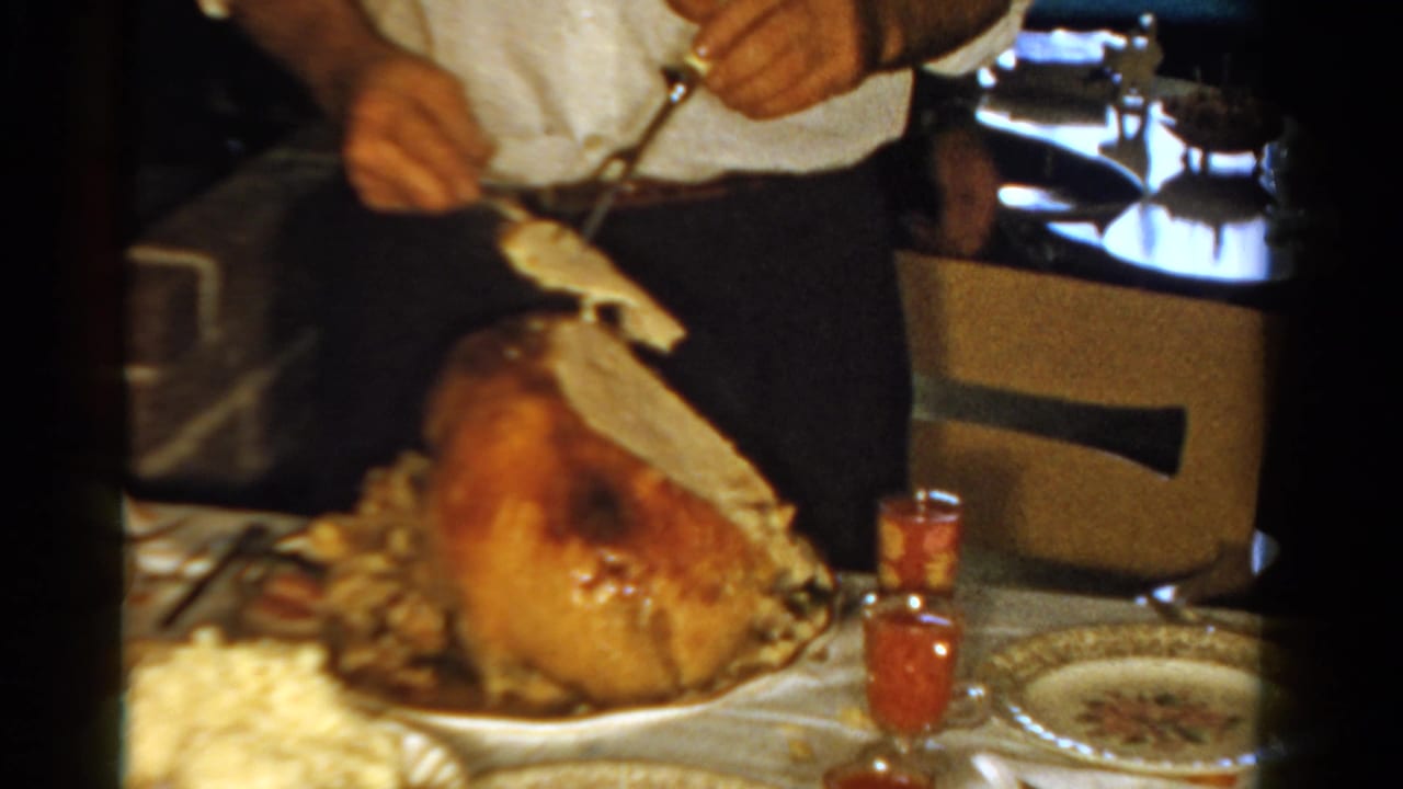 In this 1958 Ontario home-movie frame, an adult in a white shirt carves a roast turkey at a crowded holiday dinner table.
