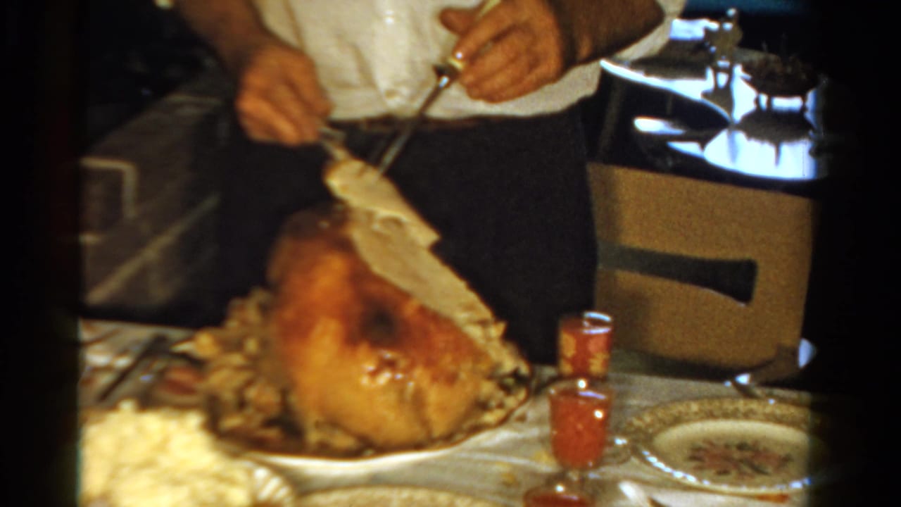 An adult carves a golden roast turkey at an Ontario dinner table, with patterned dishes and small red glasses visible nearby.