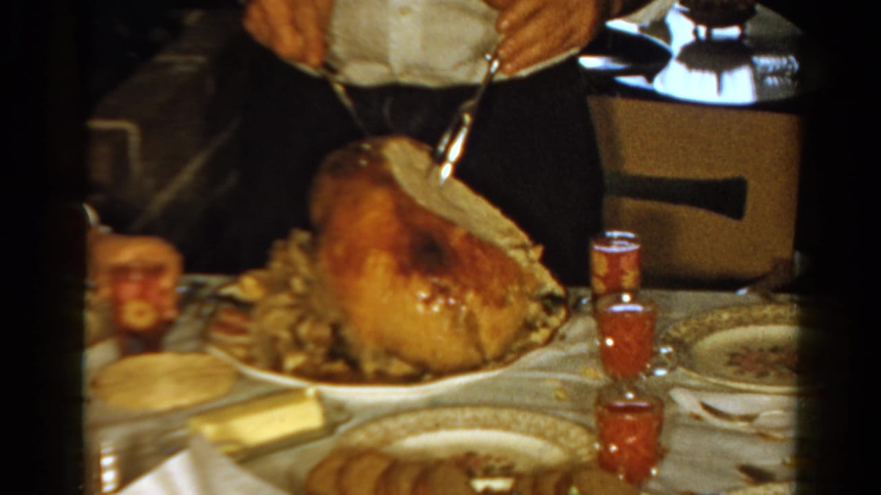 Adult hands carve a roasted turkey on a set dinner table with jelly cups and plates.