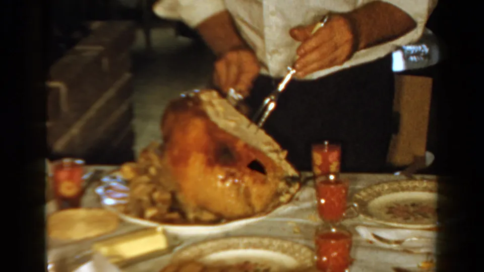 Close 8mm view of an adult carving a roast turkey at a 1958 Ontario dinner table with dishes and jelly cups visible.