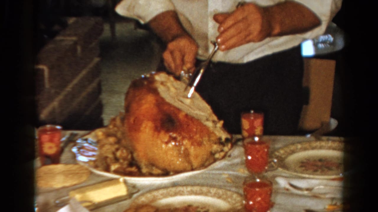1958 Ontario home-movie frame showing a person in a white shirt carving a roast turkey on a set holiday table.