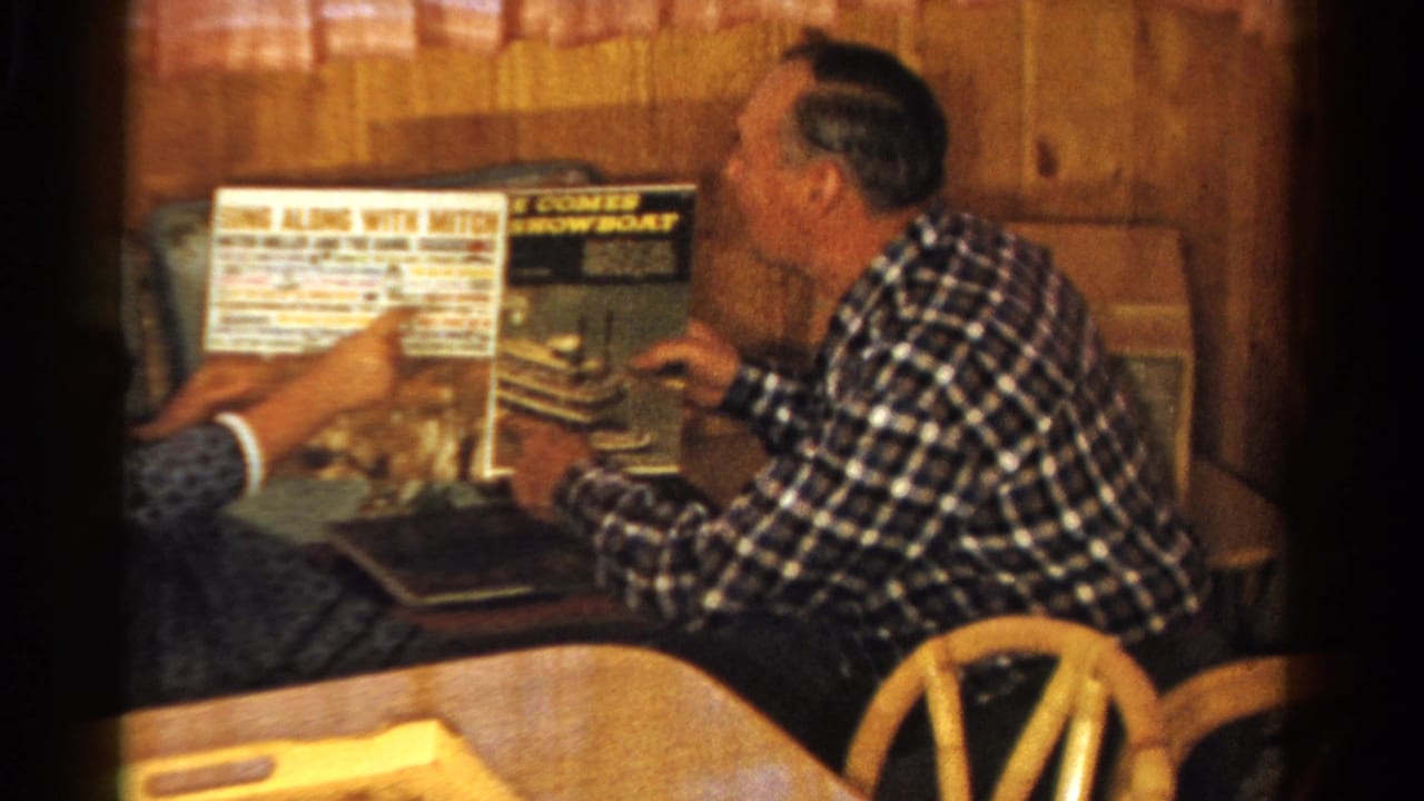 In a 1958 Ontario home interior, a seated man and companion examine record album covers in a wood-paneled room.