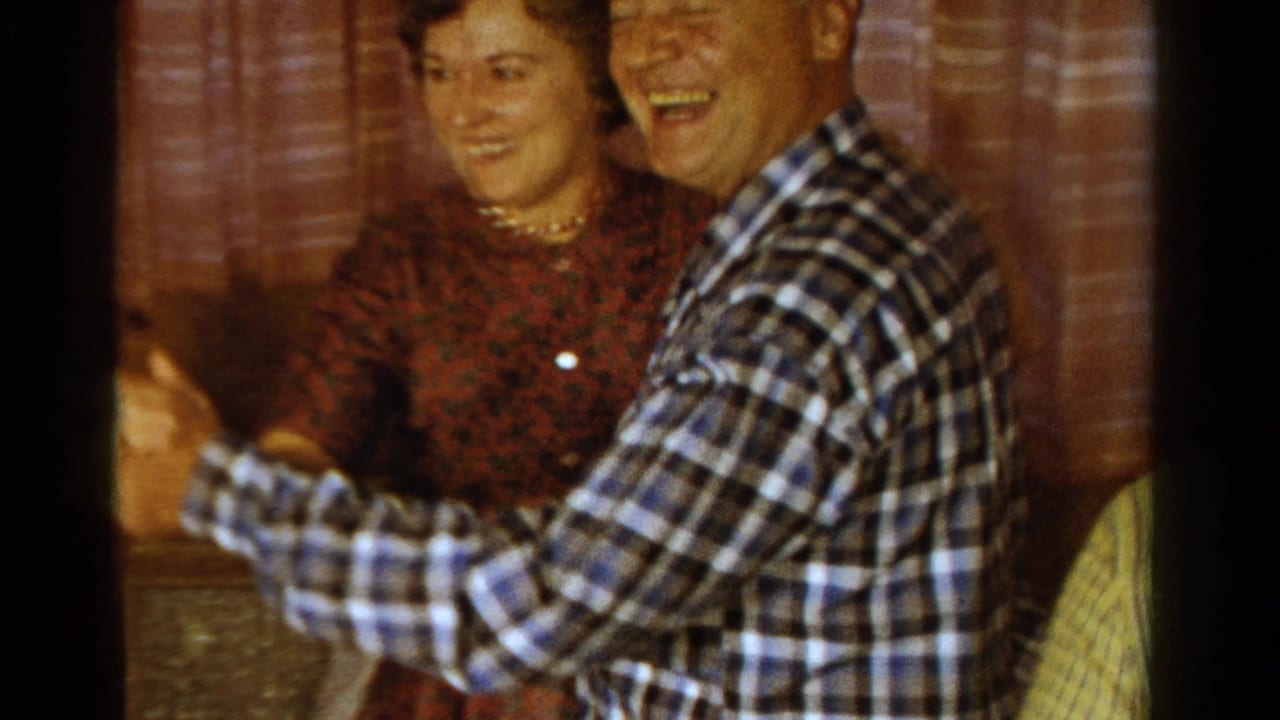Man in a plaid shirt smiles while dancing with a woman in a red dress.