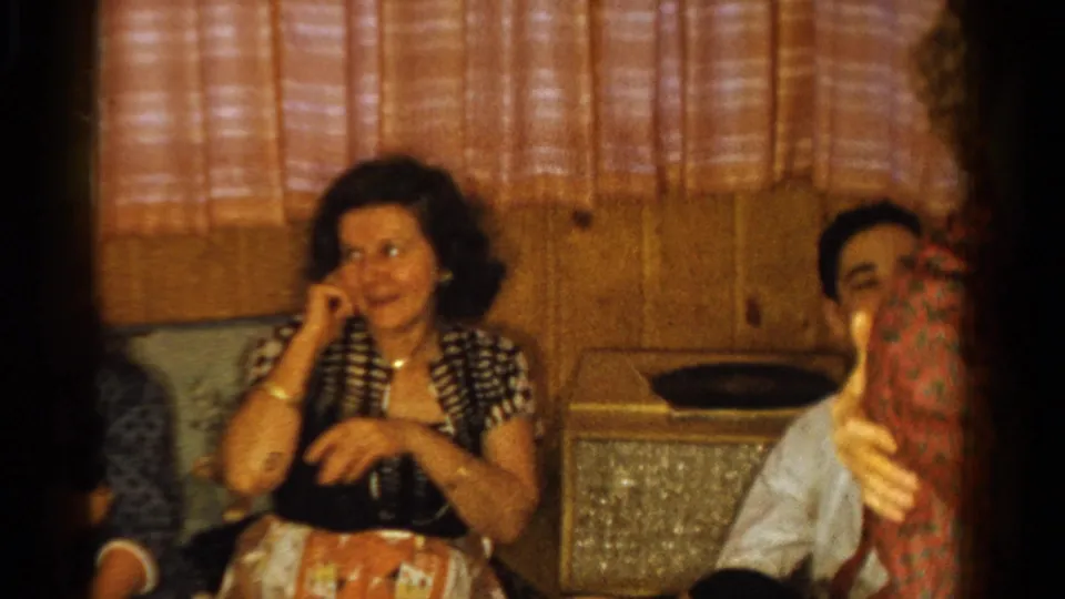 Seated guests look on from a wood-paneled room as the couple dances at the edge of this 1958 Ontario home-movie frame.