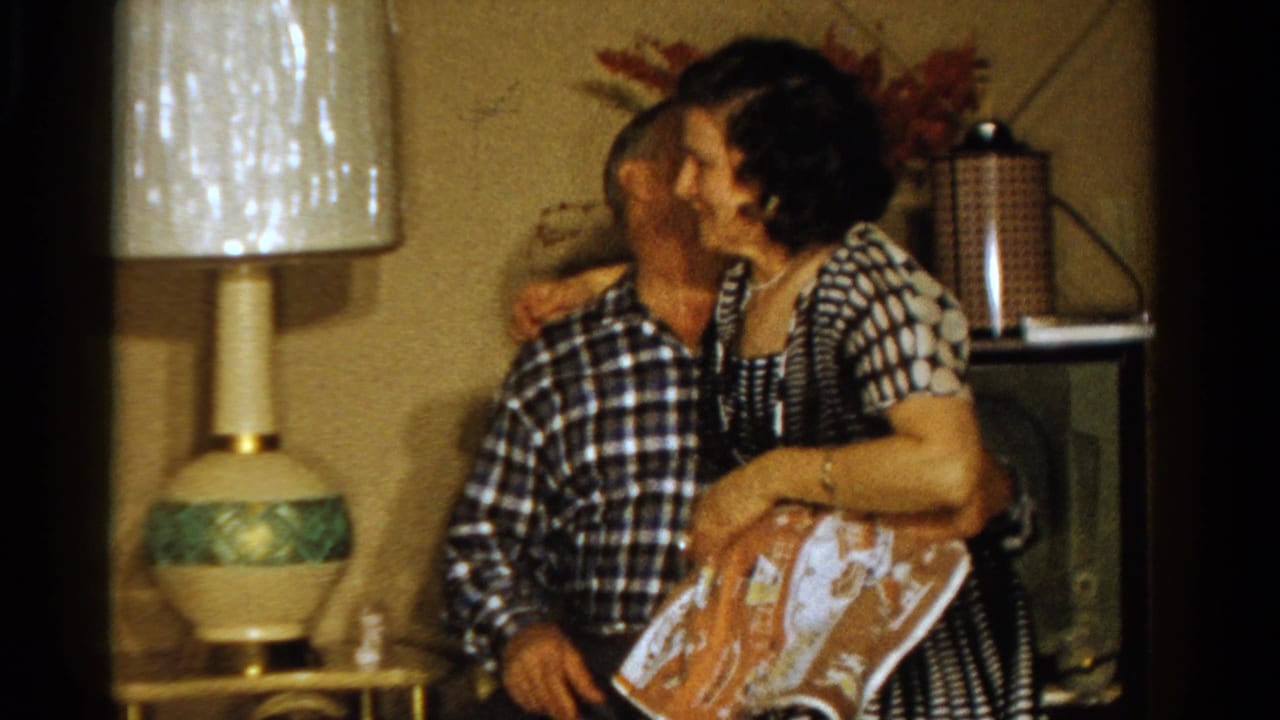 Ontario 1958 frame with a woman kissing a seated man on the cheek in a living room beside a table lamp.