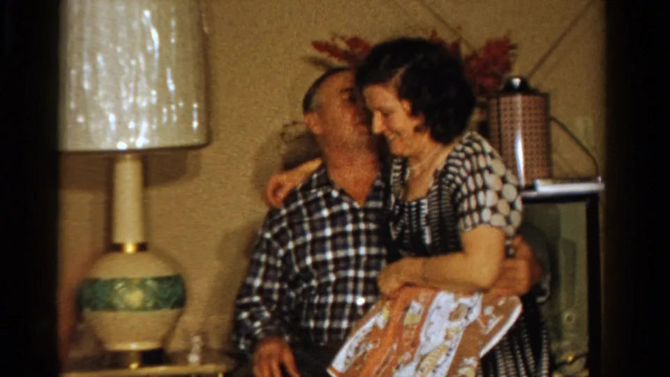 Ontario 1958 home-movie frame of a seated couple smiling and embracing near a mid-century table lamp.