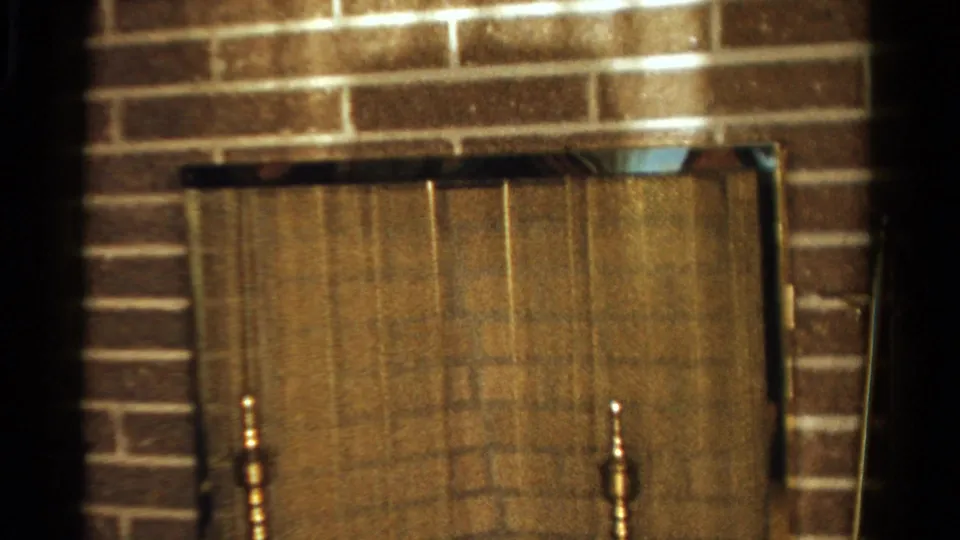 Ontario 1958 home-movie frame showing a brick fireplace and metal screen inside a private living room.