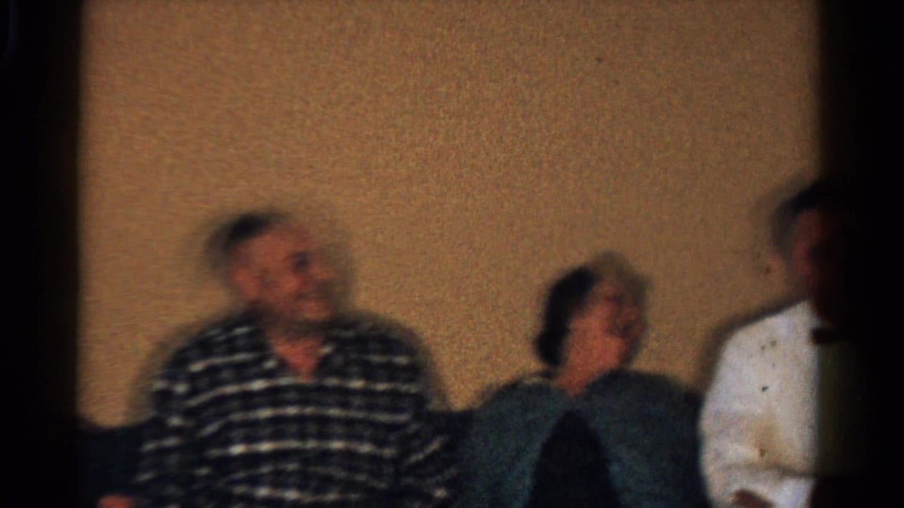 Seated adults in a warm room, including a smiling man in a plaid shirt and a woman beside him.