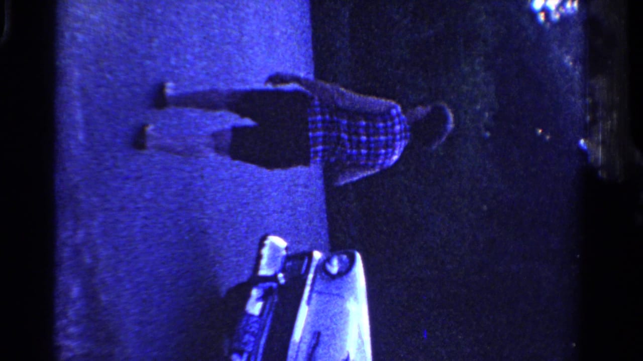 In 1958 Ontario home-movie footage, a woman walks along a paved area toward a light-colored mid-century car in strong blue illumination.