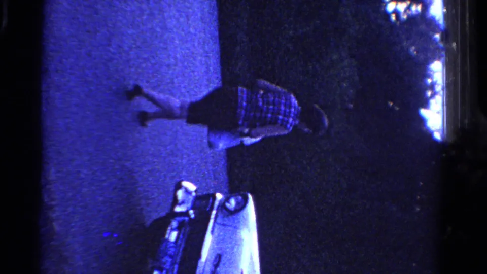 The woman moves farther along the pavement in blue light while the pale car remains partly visible below her.