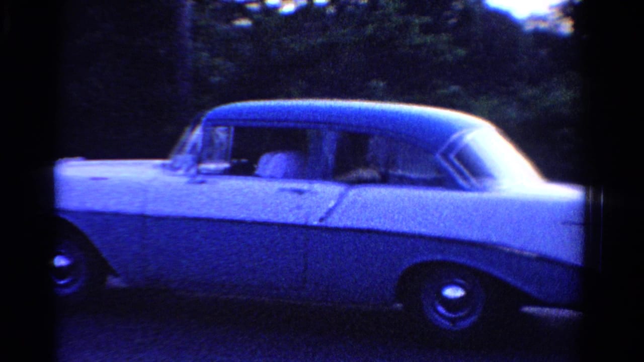 1958 Ontario home-movie frame showing a white sedan in side view along a tree-lined residential street.