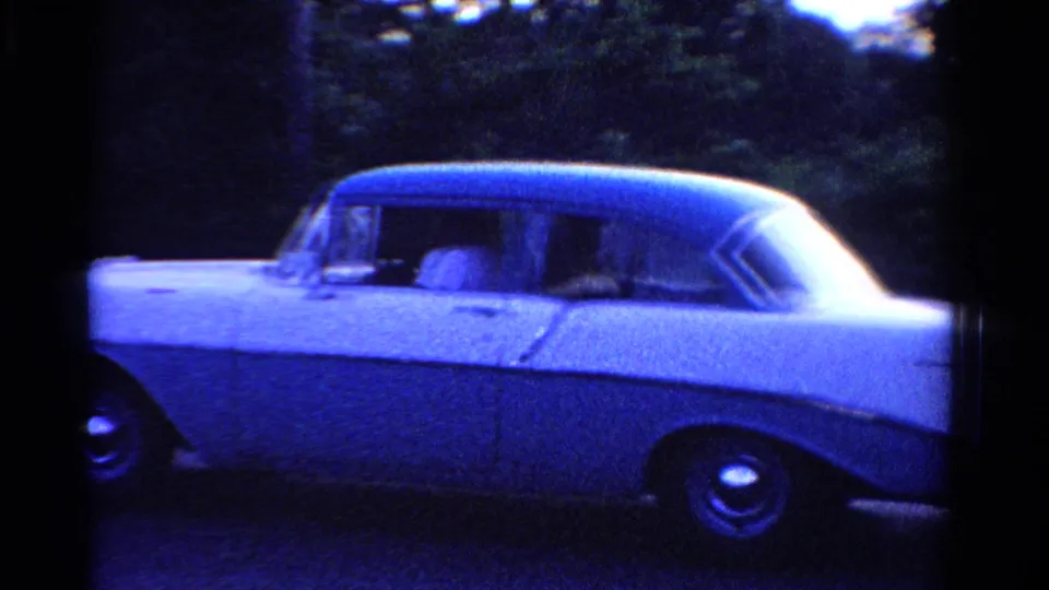 1958 Ontario home-movie frame showing a white sedan in side view along a tree-lined residential street.