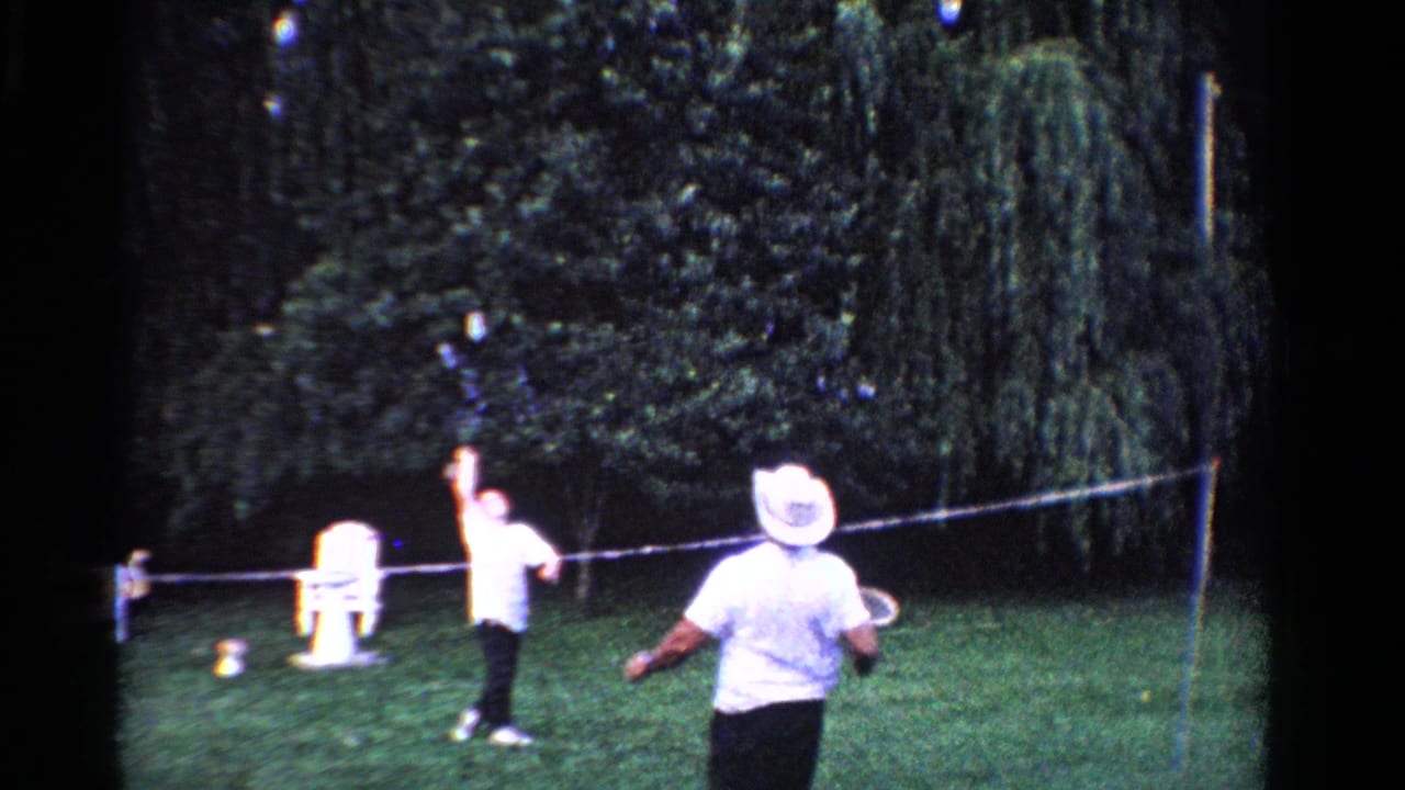 1958 Ontario backyard badminton scene with a white-hatted player in the foreground and another player near the net.