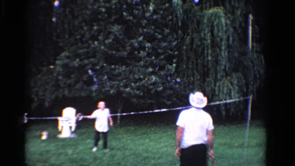 1958 Ontario home-movie frame of a backyard badminton exchange, with one player near the net and another seen from behind.