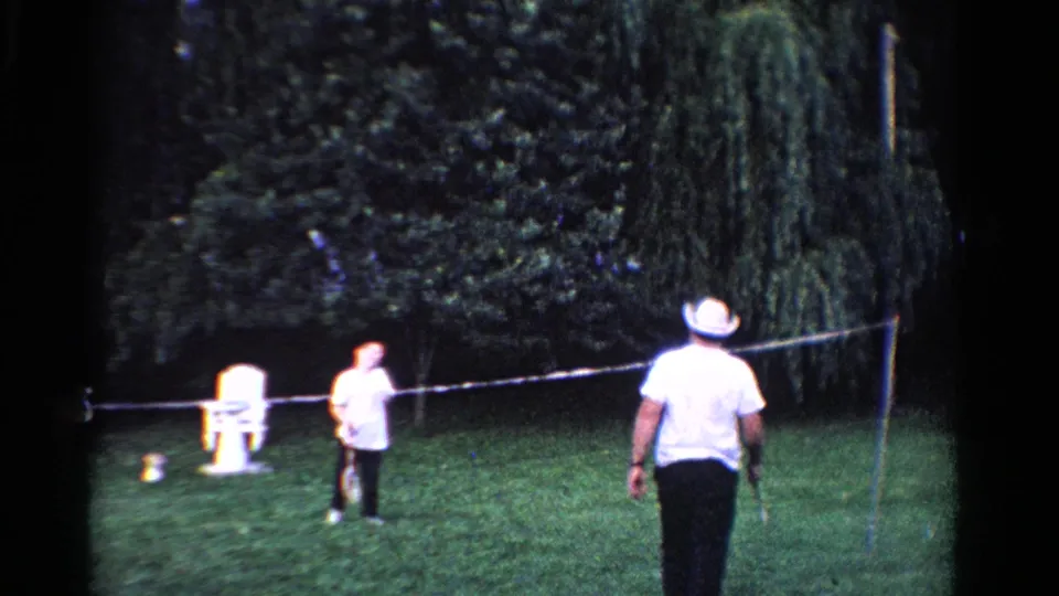 1958 Ontario backyard scene with a white-hatted badminton player moving toward the net and another player beyond it.