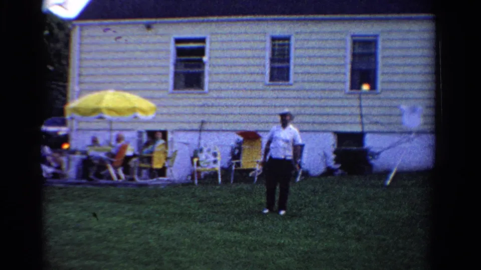 The final 1958 Ontario backyard frame shows the badminton player centered on the lawn with a patio gathering behind them.