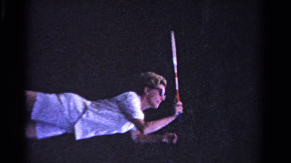 A woman in white tennis clothing raises her racket, seen in soft 8mm color on an Ontario grass court in 1958.