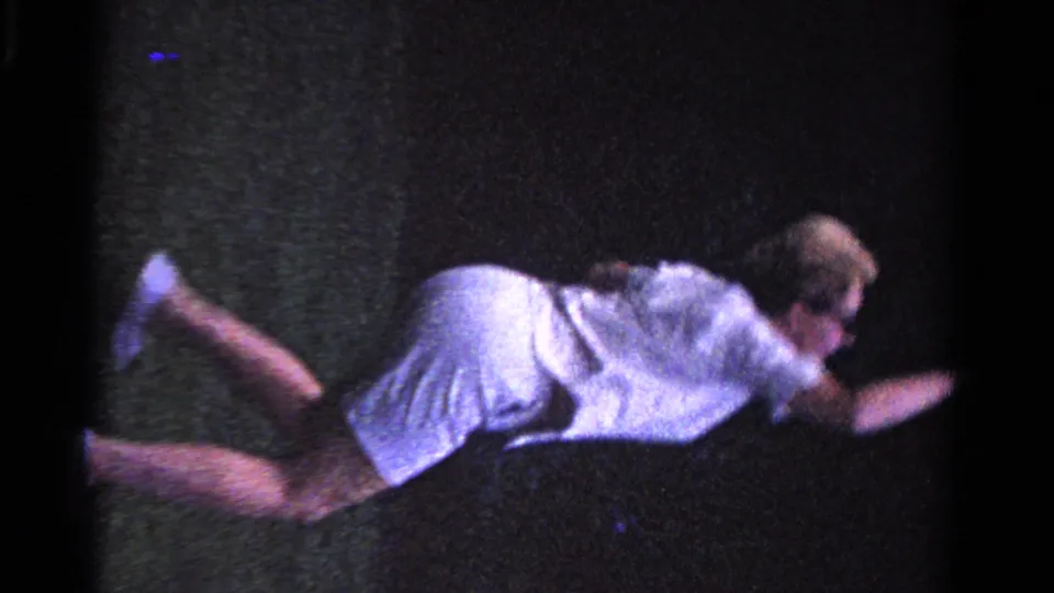 In 1958 Ontario home-movie footage, a woman in white tennis clothes leans forward on a grass court during a casual rally.