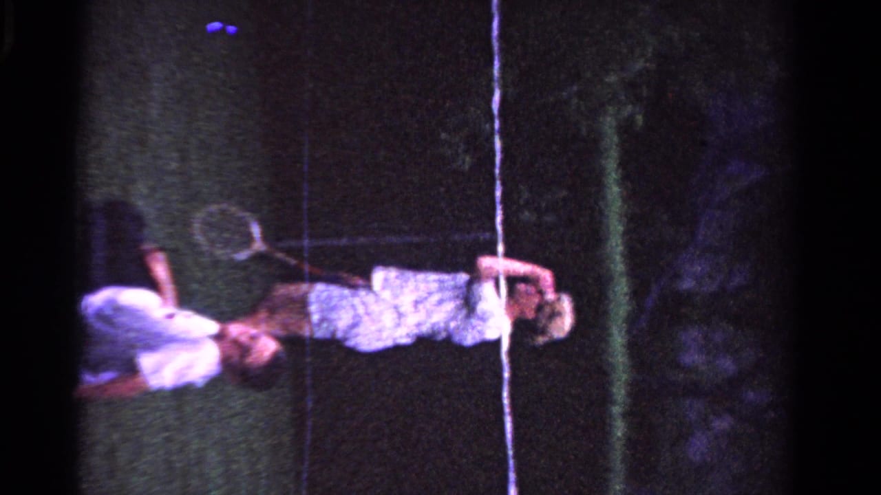 1958 Ontario frame with a man holding a tennis racket beside a woman on a grass court, with another figure low to the ground.