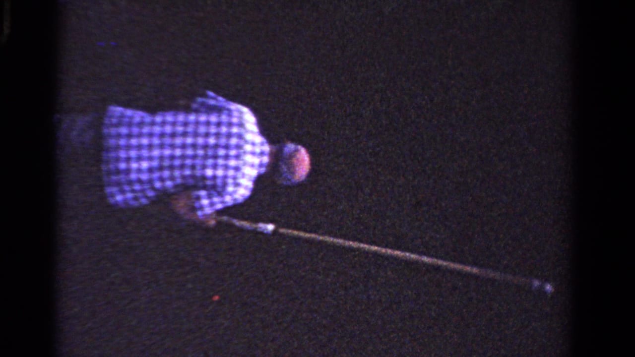 In 1958 Ontario home-movie footage, a man in a checkered shirt leans forward with a long pole in a dark outdoor setting.