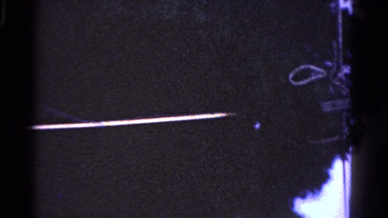 A long pole reaches across the night scene toward a looped wire or hanging object, with the person mostly out of view.