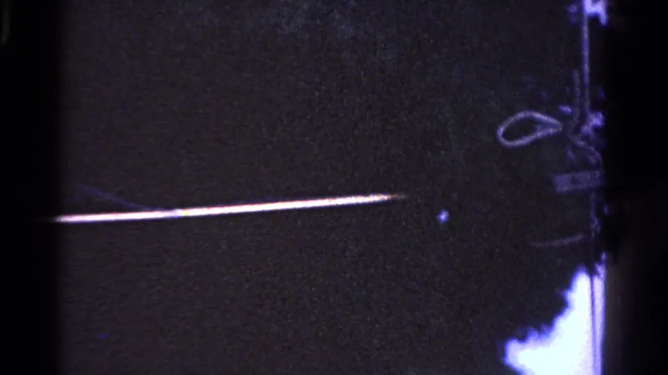 A long pole reaches across the night scene toward a looped wire or hanging object, with the person mostly out of view.
