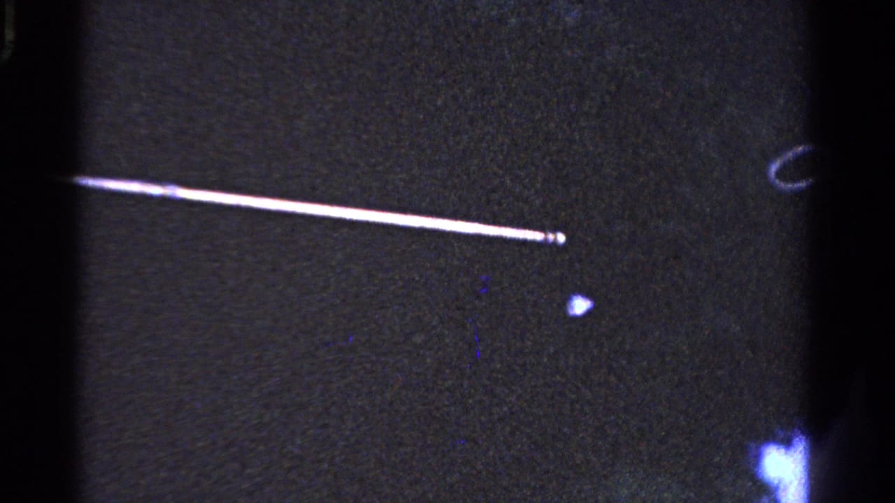 Grainy 8mm frame from the Ontario 1958 clip with a bright diagonal streak and little visible subject detail.