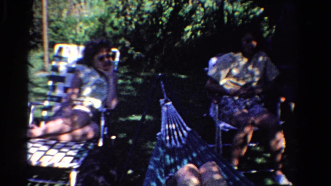 A woman sits in a lawn chair while another adult sits nearby in a shaded yard.