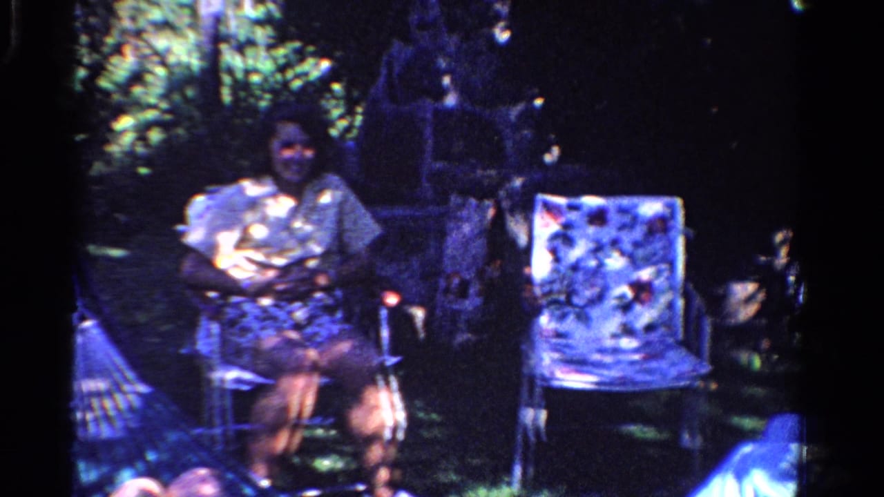 In a 1958 Ontario backyard scene, a woman sits in a folding chair near garden foliage and another patterned lawn chair.