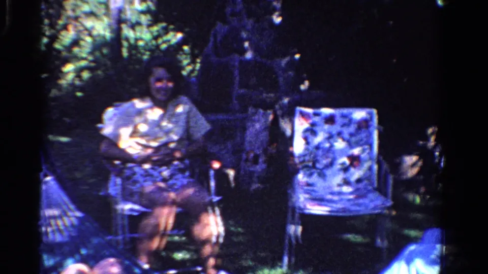 In a 1958 Ontario backyard scene, a woman sits in a folding chair near garden foliage and another patterned lawn chair.