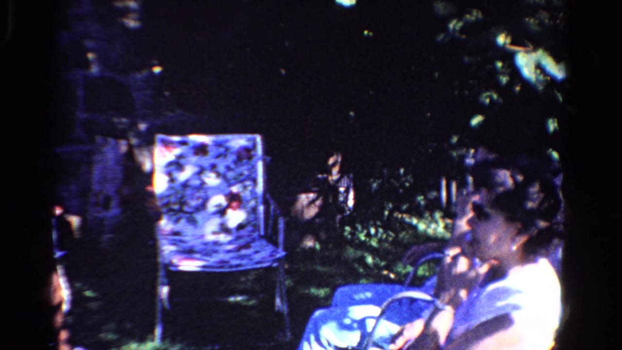 Seated woman in profile near a patterned chair and dense garden plants.