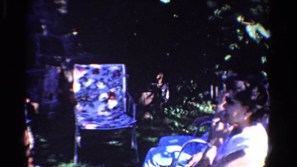 A woman sits in profile in the Ontario backyard, with a patterned lawn chair, blue fabric, and shaded foliage nearby.