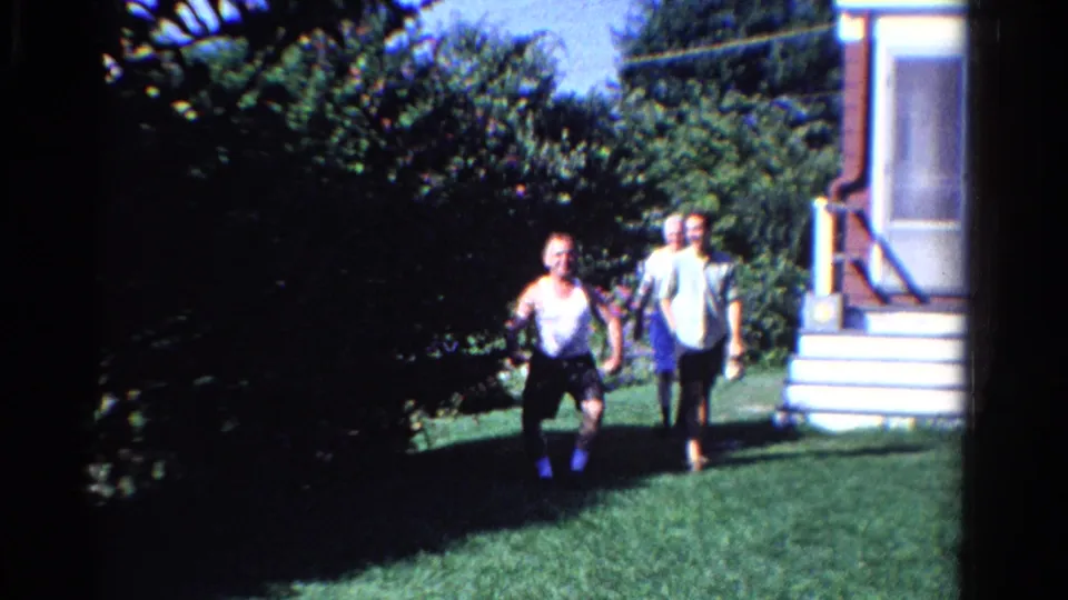 Two adults walk across a grassy Ontario backyard near dense shrubs and the steps of a house exterior.
