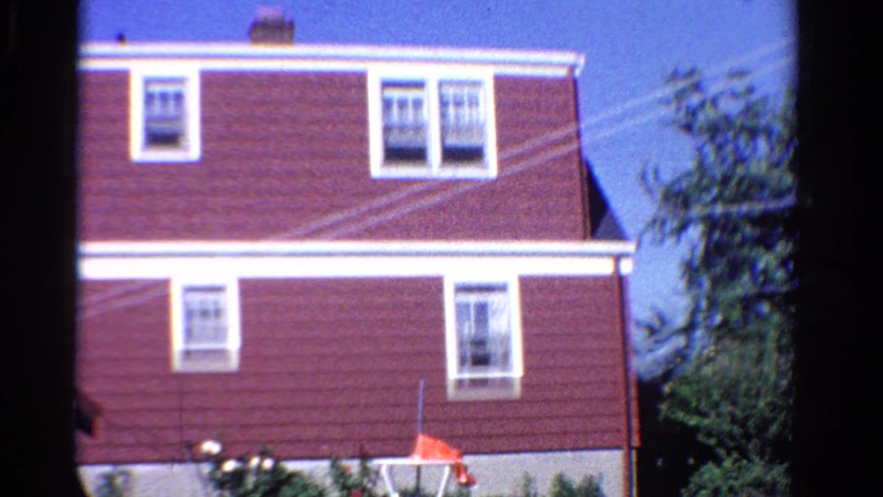 Red-sided house with white-trimmed windows under a blue sky.