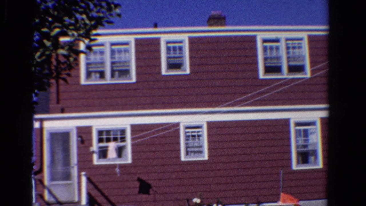 1958 Ontario 8mm frame showing a maroon two-story house with white trim, screened side door, trees, and a clothesline.