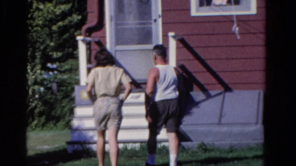 The two adults reach the front steps of the red-sided Ontario house, with lawn, shrubs, railings, and a screen door visible.