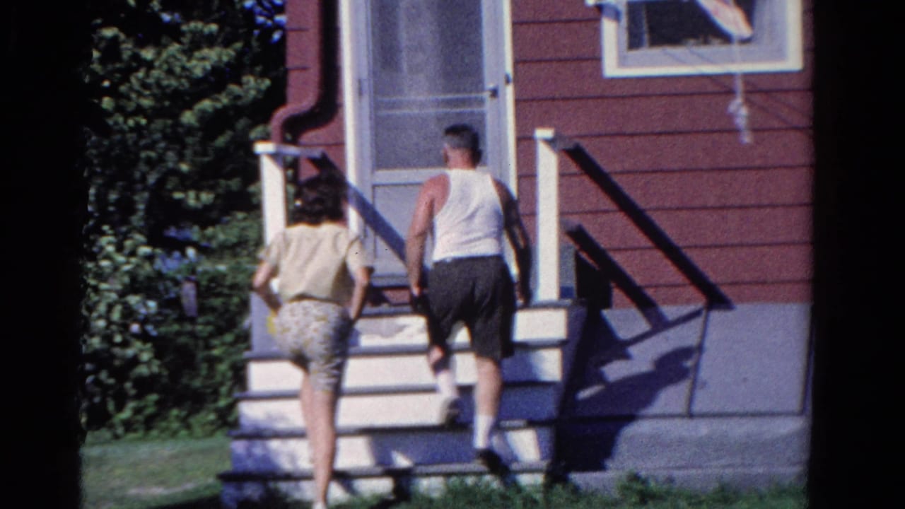 A woman and man climb the porch steps toward a screen door.