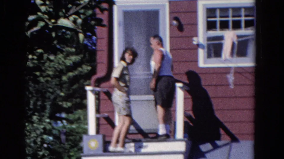 At the porch doorway, the two adults turn back toward the camera in 1958 Ontario home-movie footage.