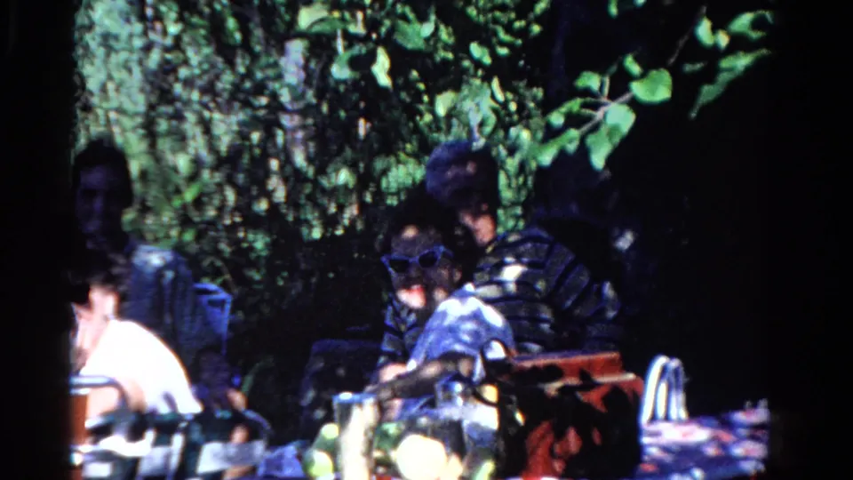 Adults at a shaded Ontario backyard picnic table in 1958, with a man in sunglasses and casual summer clothing visible.