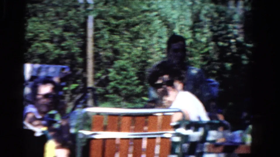 Soft 8mm frame of a backyard gathering in Ontario, with adults, lawn chairs, trees, and a round pool edge in view.