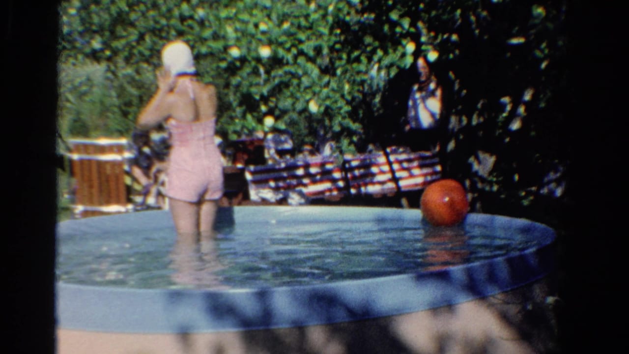 In likely 1958 Ontario home-movie footage, a woman in a pink swimsuit adjusts a white swim cap in a shallow backyard pool.