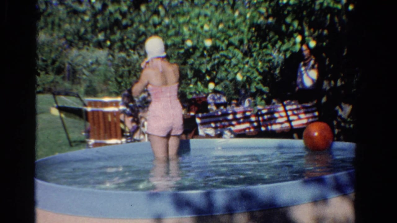 Woman stands in the pool with her back to the camera as people sit under trees.
