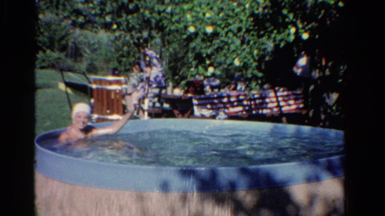 Person in a small backyard pool beside trees and lawn furniture.