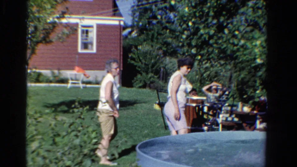 1958 Ontario backyard footage frame with adults beside a small pool, outdoor seating, trees, lawn, and a red house exterior.