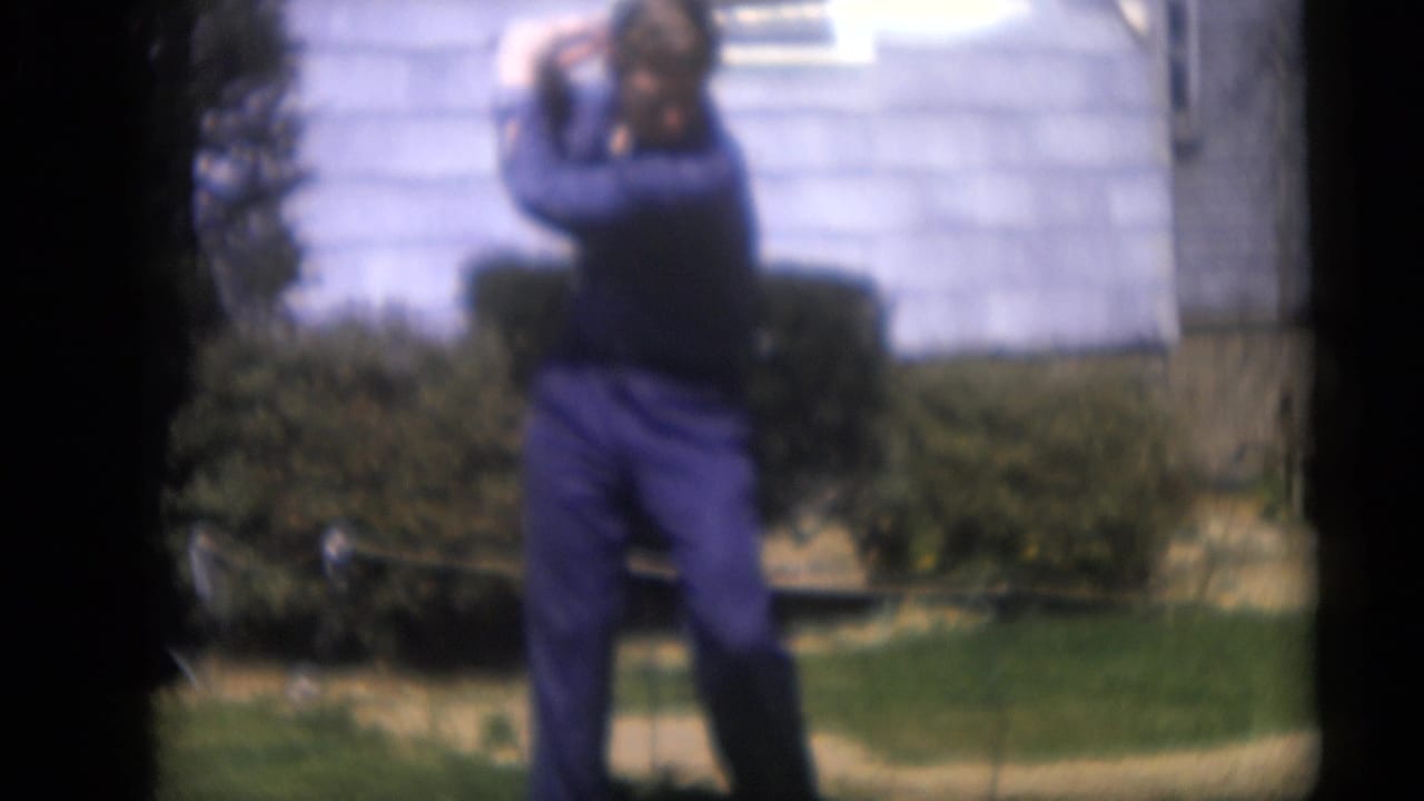 Man in blue clothing prepares to swing a golf club on a backyard lawn.