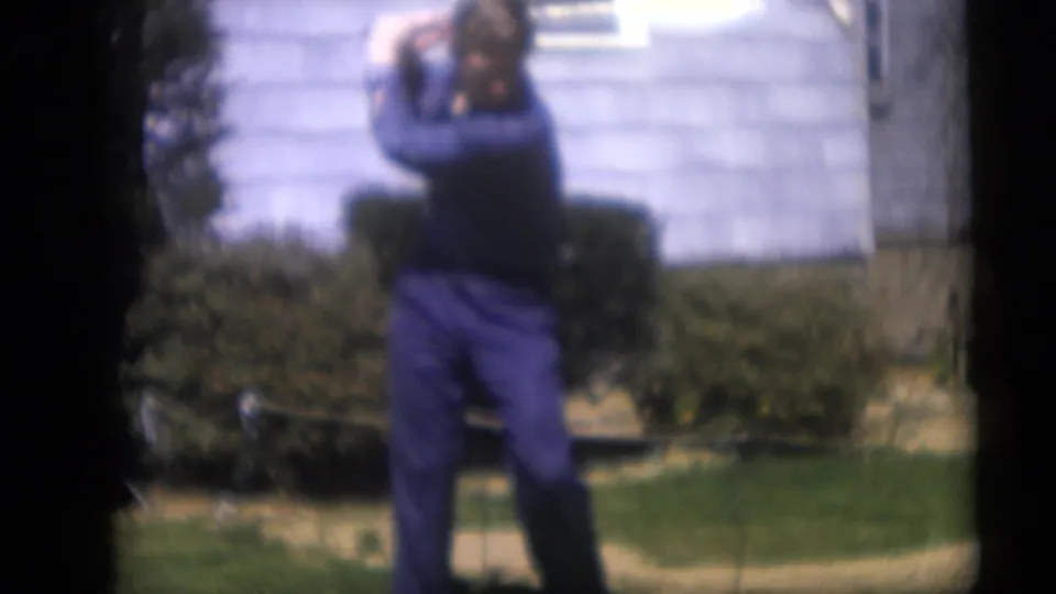 In 1959 Camden, New Jersey home-movie footage, a man in blue clothing stands on a lawn with a golf club before a light-sided house.