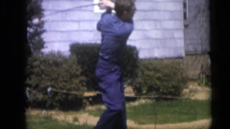 In the 1959 backyard scene, the man is seen from the side as his golf swing continues before shrubs and house siding.